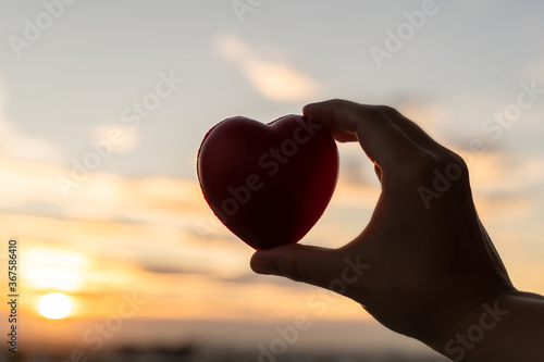 Silhouette of woman hand with red heart on blue sunset sky background. Concept