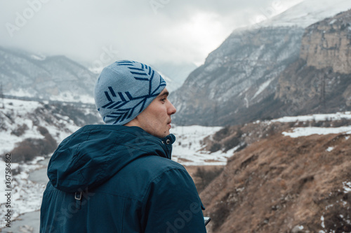Back view portrait of male adult traveller in winter clothing with Caucasus mountain range landscape in the background. Travel destination concept.