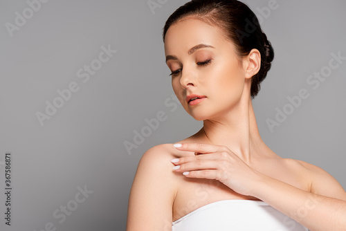 beautiful woman with perfect skin touching shoulder isolated on grey