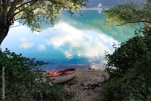 white boat on the shore of Lake Scanno, Abruzzo. Colorful reflections on the water in a summer landscape surrounded by nature. Frame of green vegetation. Glimpse of calm, tranquility and relaxation.  photo