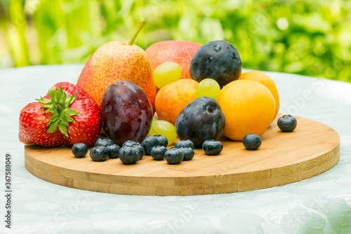 Fresh fruits and berries lie on a wooden board  the table is in a summer cottage outside the city.