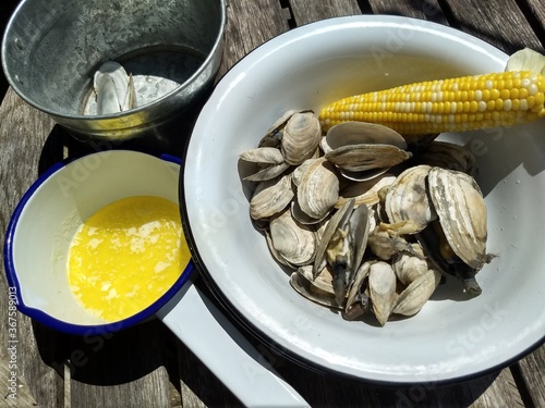 New England Steamer clams and steamed corn, in white enamel bowl, with melted butter and discard bucket