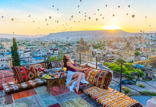 A woman have breakfast on one of the Cappadocia roof in early morning sunrise, when balloons fly. Romantic scene Cappadocia, Turkey.. photo