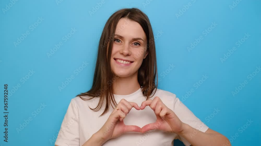 Young girl having wide charming smile put hands on chest make with fingers heart shape symbol of charity and human kindness, isolated on blue studio background. Generosity liberality sign concept Young girl having wide charming smile put hands on chest make with fingers heart shape symbol of charity and human kindness, isolated on blue studio background. Generosity liberality sign concept