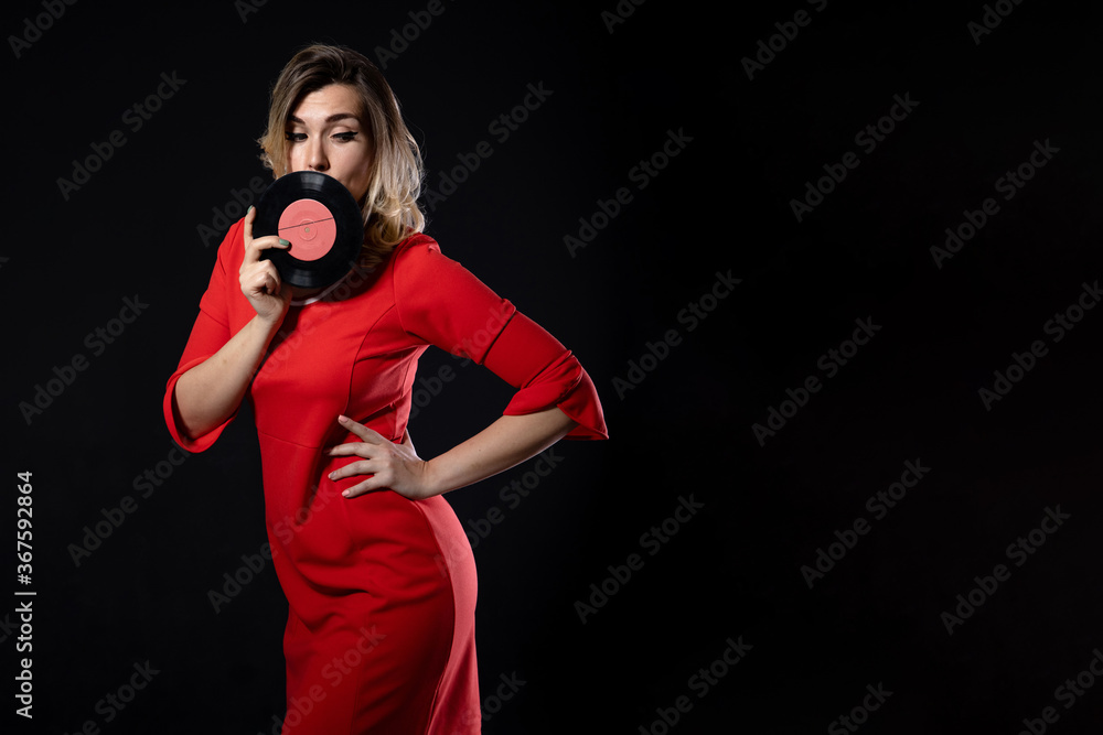 Obraz premium blonde girl in a red dress with vinyl records in hands on a black background with copy space