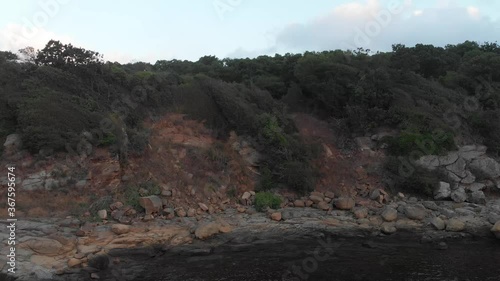 Rocky coastline of the sea at the foot of a steep high cliff, which ends with a dense forest.