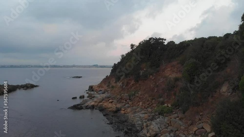 Rocky coastline of the sea at the foot of a steep high cliff, which ends with a dense forest.