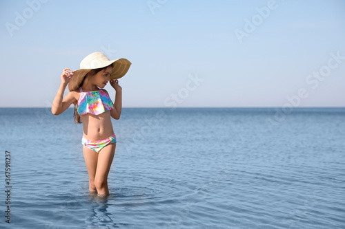 Cute little child with straw hat in sea on sunny day. Beach holiday
