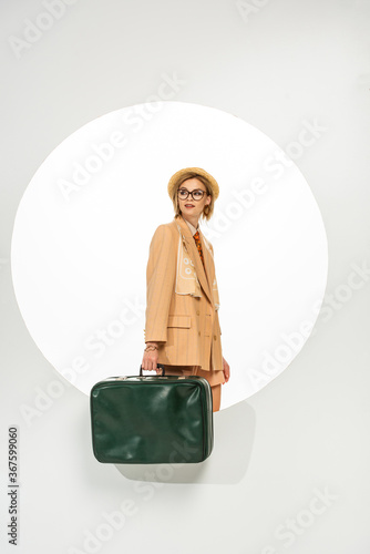 Beautiful stylish girl holding green travel bag near circle on white background