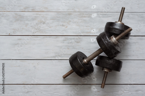 Old black dumbbells on a wooden floor background. Simple gym flat lay background with copy space.