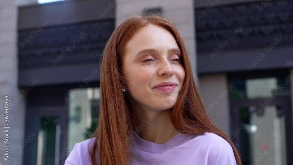 Close-up of face of smiling redhead girl looking around, background of modern city street. Portrait of beauty young woman feeling happy outdoors. Cheerful lady standing on urban outside. closeup. Close-up of face of smiling redhead girl looking around, background of modern city street. Portrait of beauty young woman feeling happy outdoors. Cheerful lady standing on urban outside. closeup.
