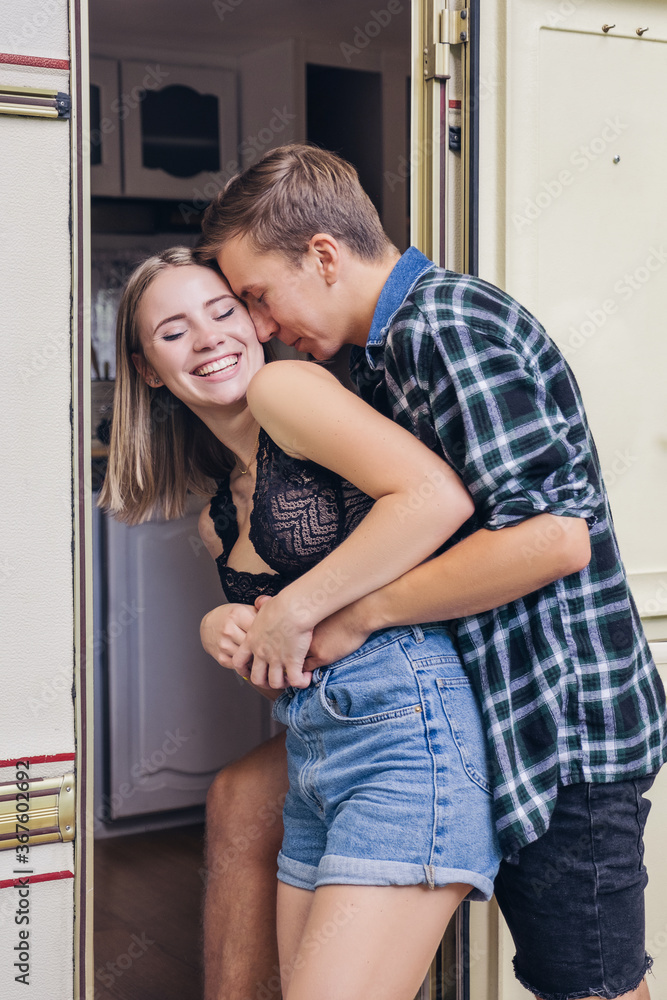 Cute young couple in love near cabin house. They hugging and kissing and are sweet and caring to each other. Summer daylight portrait in casual outfit, outdoors. Copy space