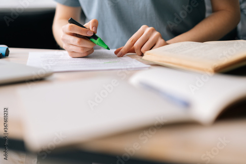 Close-up of hands of unrecognizable businesswoman highlighting important things in paper document with marker. Business lady working at home office.