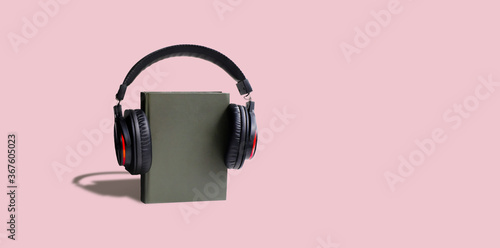 book in headphones on pink background .audiobook concept