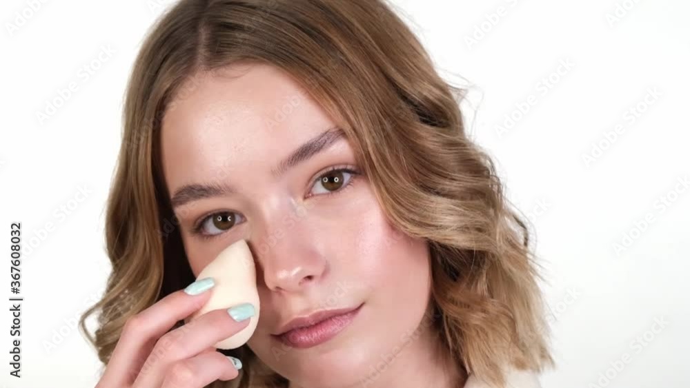 Beautiful tender young girl in a white home bathrobe with clean fresh skin posing in front of the camera with a sponge in her hands. Beauty face. Skin care. Beautiful tender young girl in a white home bathrobe with clean fresh skin posing in front of the camera with a sponge in her hands. Beauty face. Skin care.