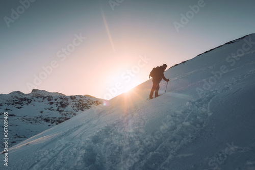 Man mountaineer with trekking pole climbing on snowy hill and sunshine at Ryten mount photo