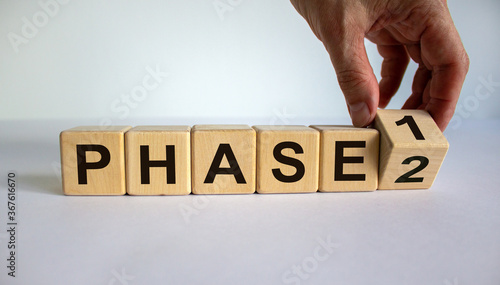 Time for Phase 2. Hand is turning a cube and changes the word 'Phase 1' to 'Phase 2'. Beautiful white background. Business concept. Copy space. photo