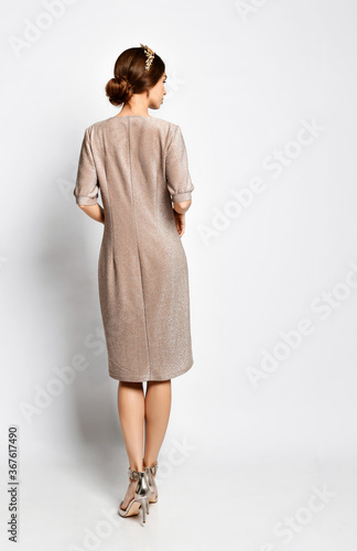 Back view of woman in elegant tiara, sparkling light rose dress with sleeves down to elbows and glossy high heels. Full length shot isolated on white