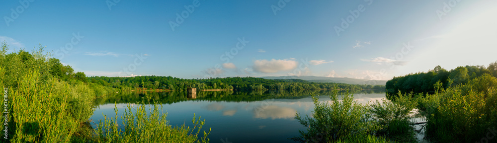 Panoramic landscape from the lake with colorful clouds in the summer sun.