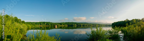 Panoramic landscape from the lake with colorful clouds in the summer sun.