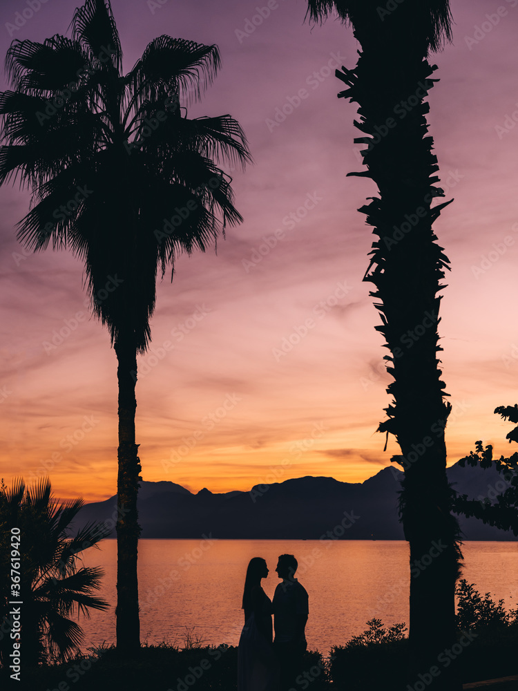 Silhouettes of young couple on sunset background