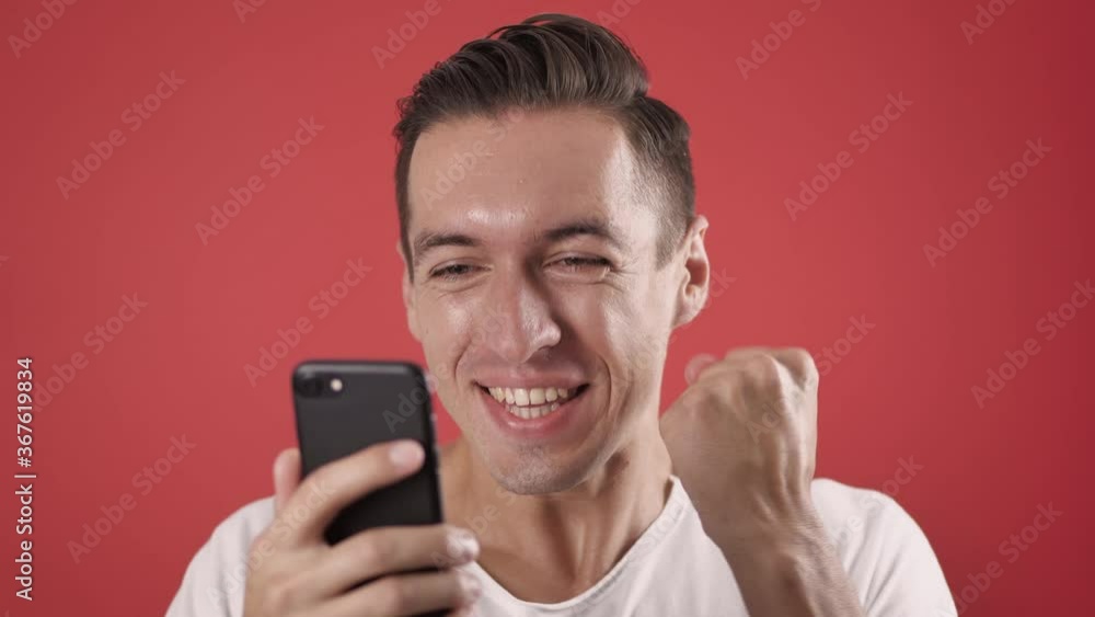 Excited man winner hold smartphone feel amazed overjoyed with mobile online bet bid app game win on red background, happy ecstatic male user use look at mobile phone celebrate read good news Excited man winner hold smartphone feel amazed overjoyed with mobile online bet bid app game win on red background, happy ecstatic male user use look at mobile phone celebrate read good news