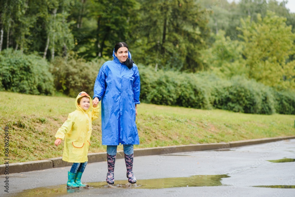 Fototapeta premium Mother and child, boy, playing in the rain, wearing boots and raincoats