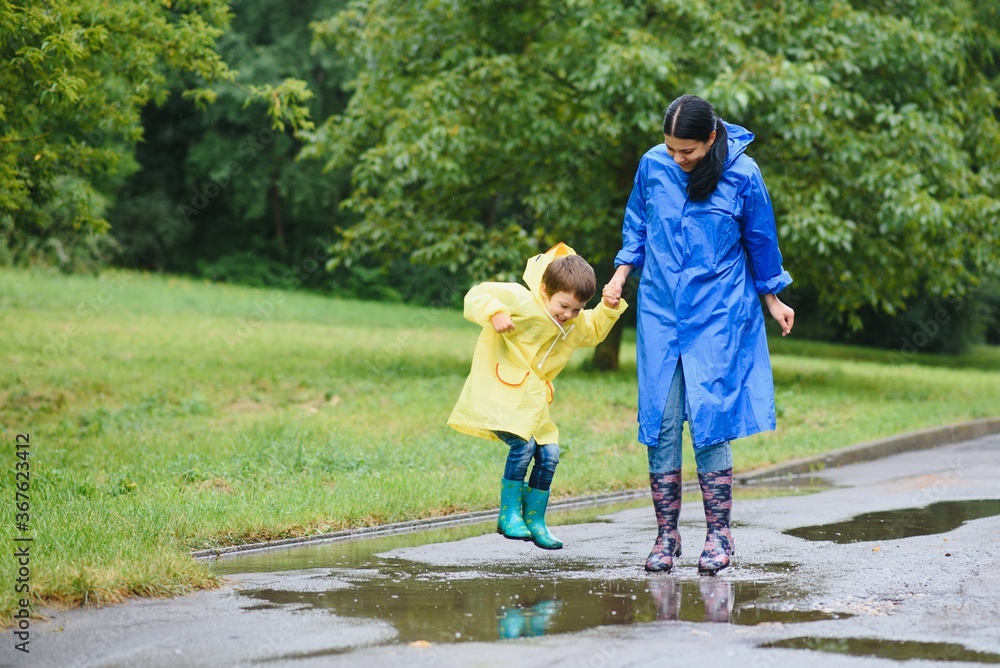 Mom and son in raincoats have fun together in the rain. concept of family vacation and happy childhood. Mom and son in raincoats have fun together in the rain. concept of family vacation and happy childhood.