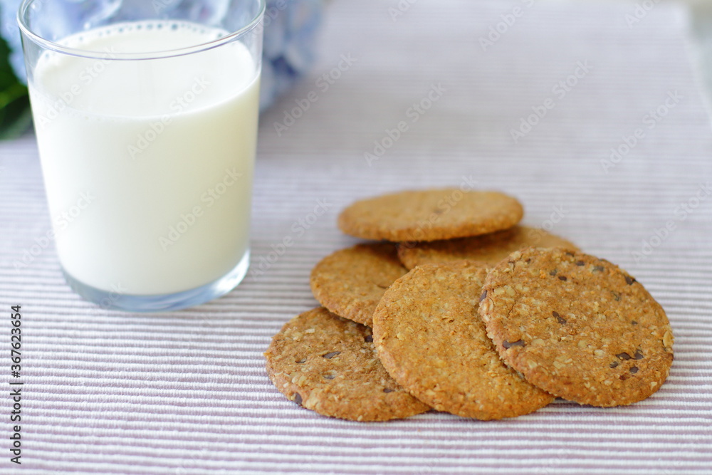 Oat cookies with glass of milk for breakfast on table cloth and blue flower on background, rustic healthy food Oat cookies with glass of milk for breakfast on table cloth and blue flower on background, rustic healthy food