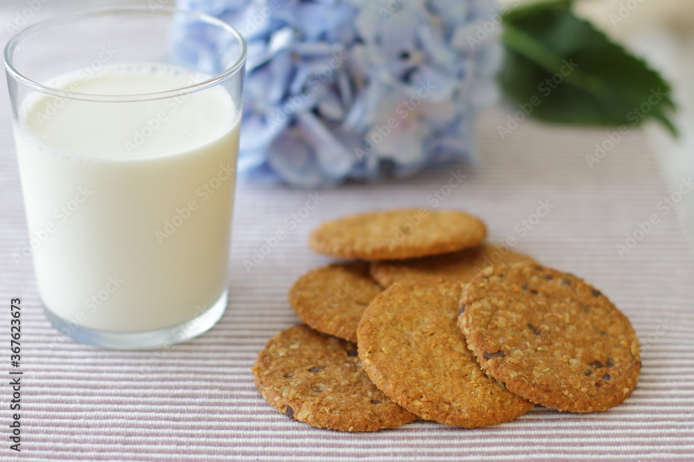 Oat cookies with glass of milk for breakfast on table cloth and blue flower on background, rustic healthy food Oat cookies with glass of milk for breakfast on table cloth and blue flower on background, rustic healthy food