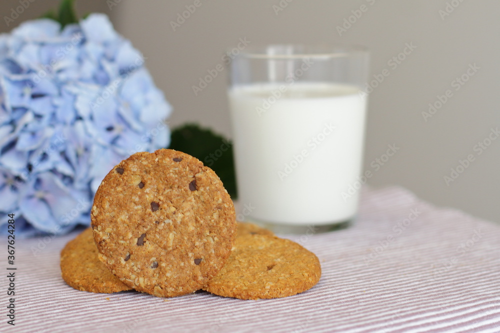 Oat cookies with glass of milk for breakfast on table cloth and blue flower on background, rustic healthy food Oat cookies with glass of milk for breakfast on table cloth and blue flower on background, rustic healthy food