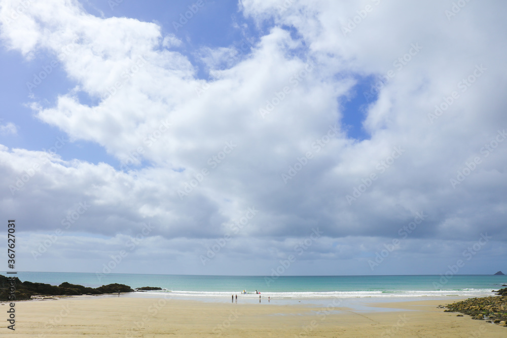 Cornwall beach on Porthluney Bay with cloudy blue sky and horizon over the water