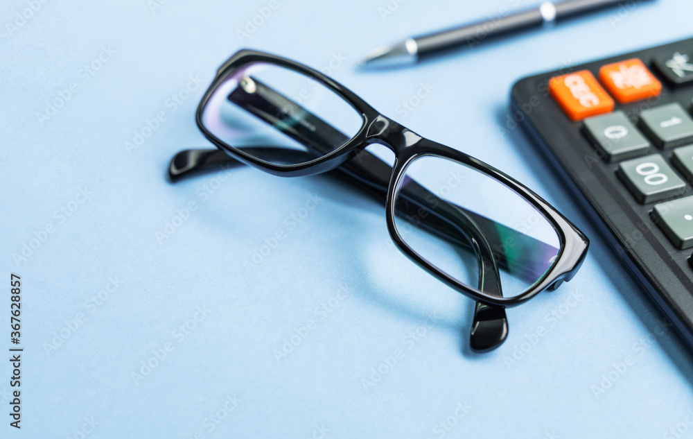 Close up of calculator, pen and glasses on blue background for mockup design modern lifestyle stationary concept. Office table with supplies. Modern office desk Workspace Working background concept Close up of calculator, pen and glasses on blue background for mockup design modern lifestyle stationary concept. Office table with supplies. Modern office desk Workspace Working background concept