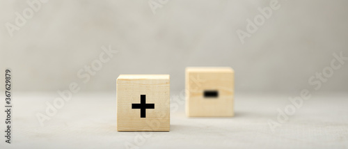 cubes with PLUS symbol in focus and MINUS out of focus on paper surface in front of concrete background