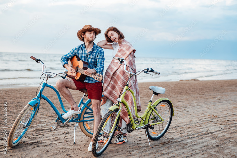 Two attractive people are standing with their bicycles. Boy is looking at the girl