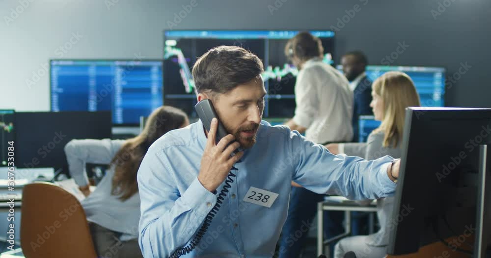 Caucasian handsome male broker working at computer in trading office and answering phone calls on many telephones. Trader buying and selling while talking with clients and working hard. Trade job. Caucasian handsome male broker working at computer in trading office and answering phone calls on many telephones. Trader buying and selling while talking with clients and working hard. Trade job.