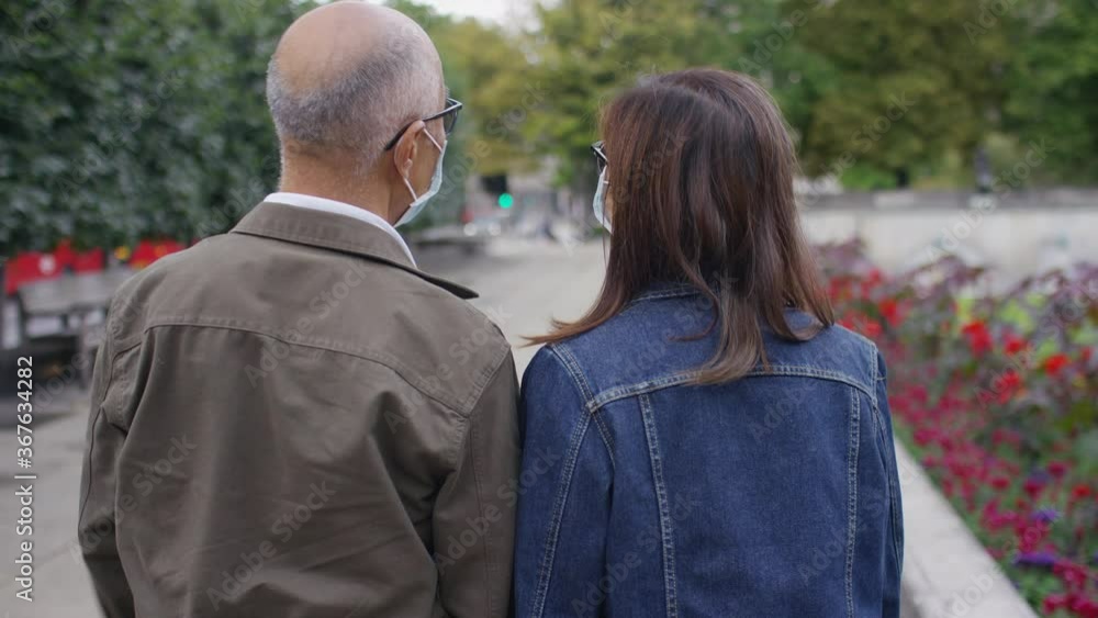 Camera follows a senior Chinese couple wearing face masks as they walk through a quiet city, in slow motion Camera follows a senior Chinese couple wearing face masks as they walk through a quiet city, in slow motion