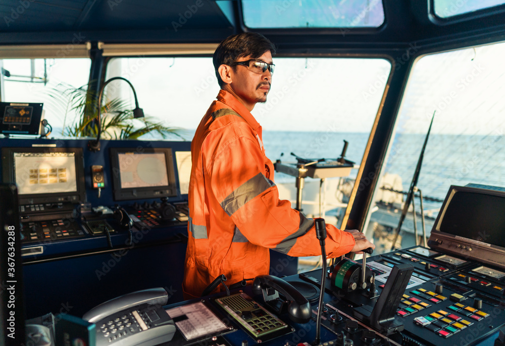 © Igor Kardasov - Filipino deck Officer on bridge of vessel or ship wearing coverall during navigaton watch at sea . He is maneuvering with cpp thrusters propulsion