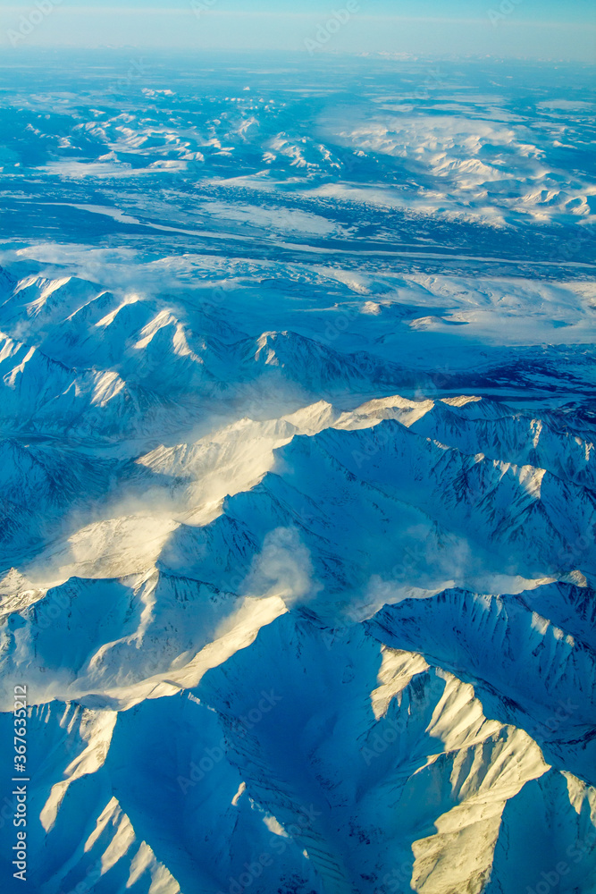 An aerial view of snow covered mountain ranges on a cold winter morning between Red Devil and Nome Alaska