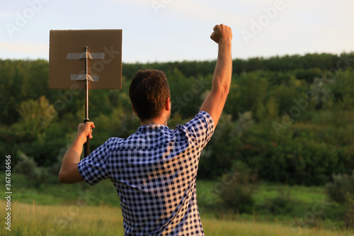 Man walkst hrough the park to protest. In his hand he holds a periscopic baton to which a cardboard plaque is attached photo