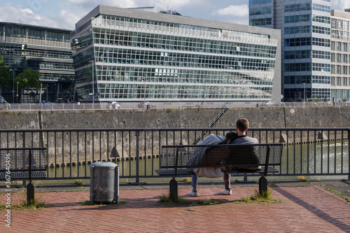 People sit on the bench enjoy sunny view at Medienhafen, harbour on Rhein River, and background of extraordinary architectures which designed by Frank Gehry in Düsseldorf, Germany.