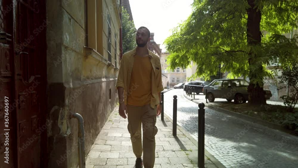 Front view of adult male traveler in yellow shirt walks along a narrow old street. Tourism during quarantine Front view of adult male traveler in yellow shirt walks along a narrow old street. Tourism during quarantine