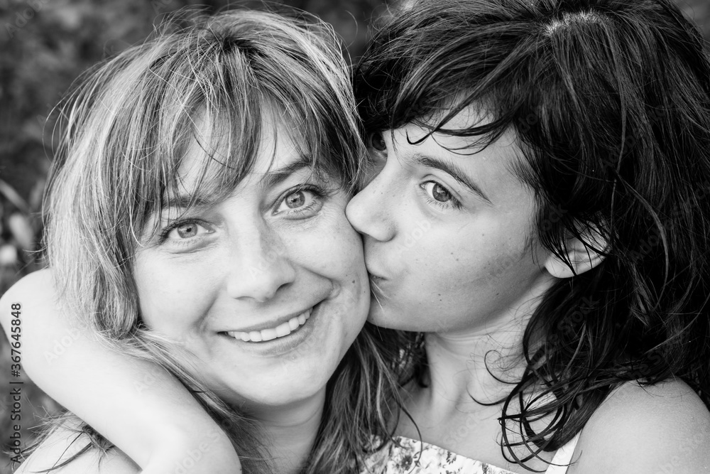 A young woman in close-up black and white portrait kissing her daughter. A young woman in close-up black and white portrait kissing her daughter.