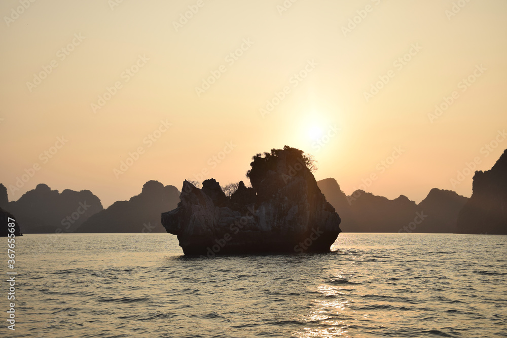 Halong Bay (UNESCO World Heritage) during a cloudless sunset with outlines of the beautiful karst landscape and a tiny island, Vietnam