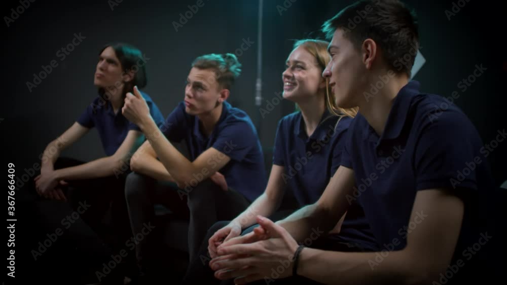 Group of three young men and one woman wearing dark blue T-shirts watching game presentation Group of three young men and one woman wearing dark blue T-shirts watching game presentation