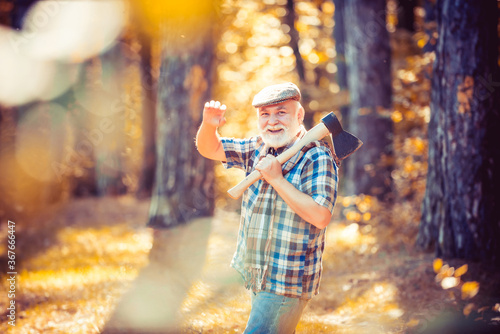 Old bearded man outdoors. Portrait of aged man with beard. Smiling old man with axe. Hiking in deep wood. Funny forester in hat in forest. Elderly male walk in forest.