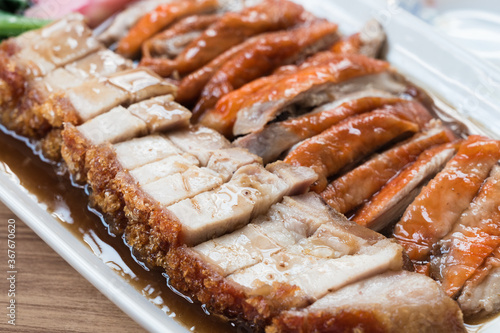 Juicy crispy pork and roasted duck in a white dish on a wooden table. Close up