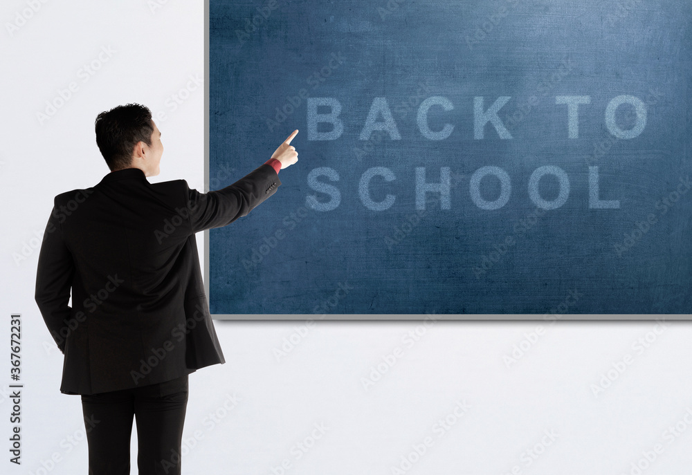 Rear view of Asian teacher man pointing chalkboard with Back to School text Rear view of Asian teacher man pointing chalkboard with Back to School text