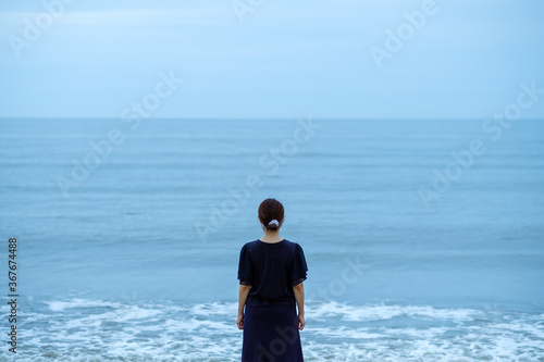 波打ち際に立つ日本人女性 後ろ姿 雨天 