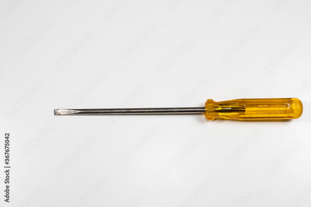 A flat-head screwdriver with handle yellow and lomg end. on a mottled white surface A flat-head screwdriver with handle yellow and lomg end. on a mottled white surface